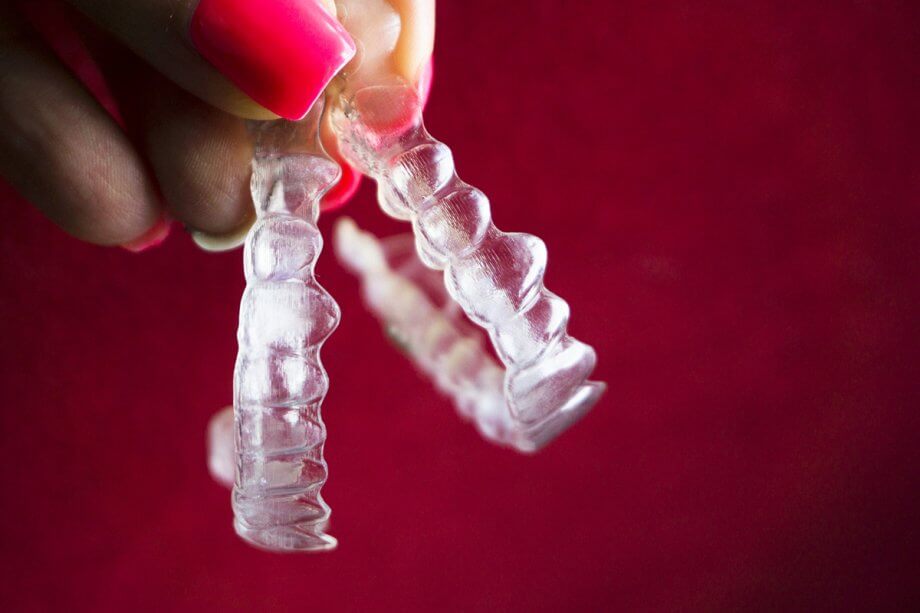 two Invisalign aligners dangle from hand