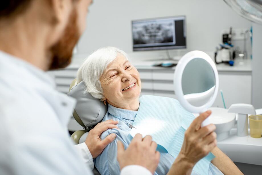 woman smiles into hand mirror from dental chair