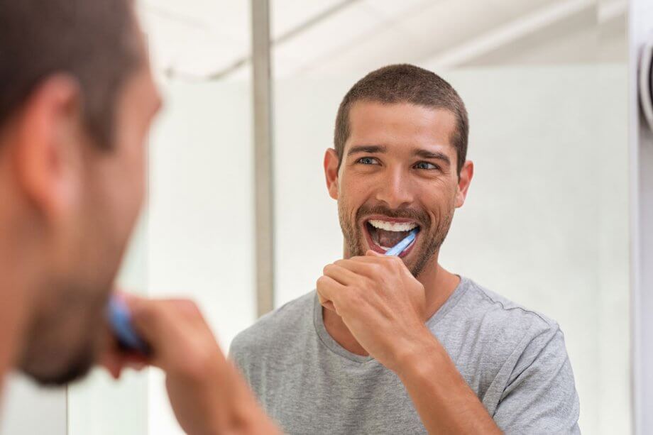 man brushing teeth in mirror