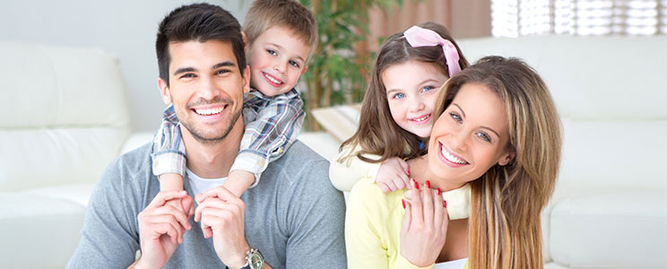 Photograph of a happy male & female couple smiling and laughing as two small children are smiling and hugging them.